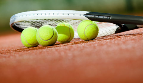 Close up of tennis racquet and balls on the clay tennis court